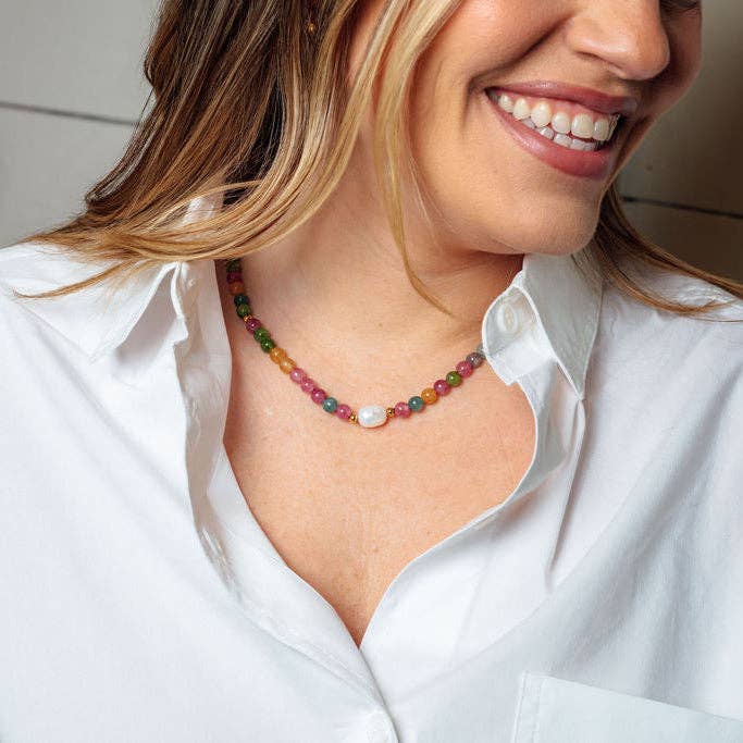 A close-up lifestyle shot of a woman wearing a colorful beaded necklace with a white pearl accent, styled with a white button-down shirt.