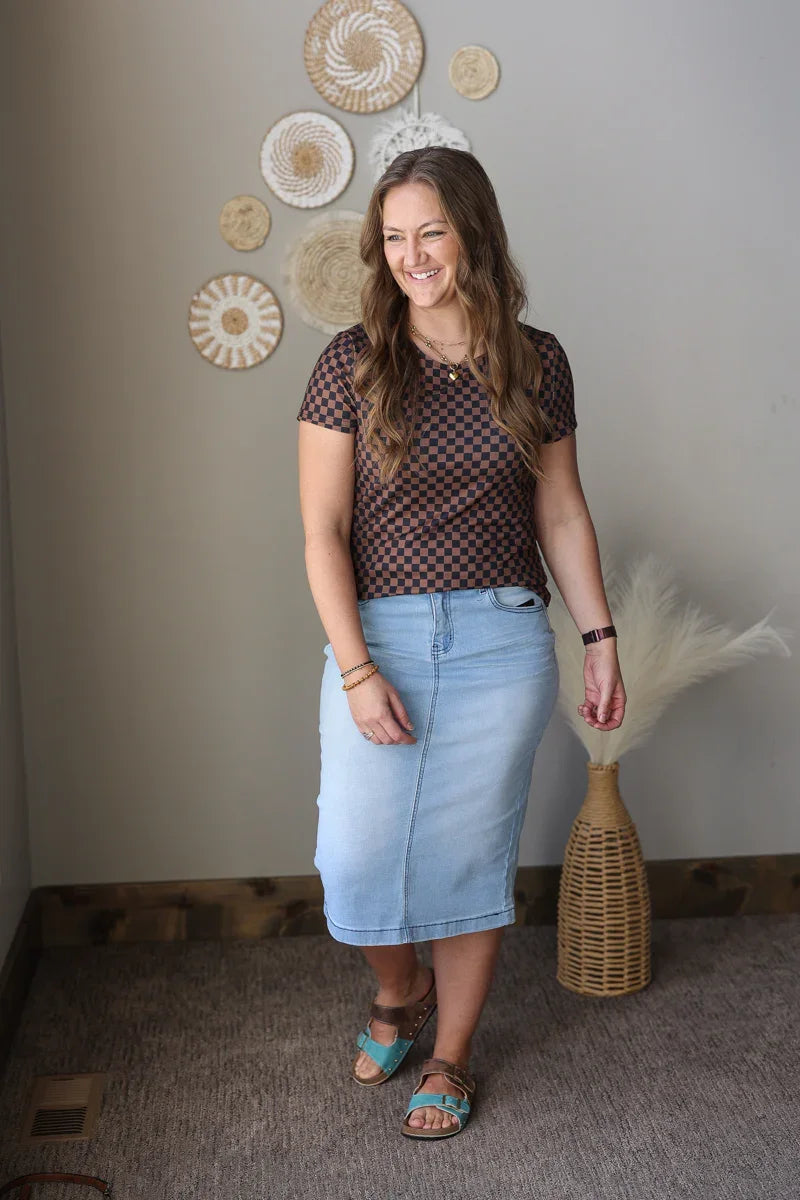 Woman wearing a patterned top and denim skirt standing in a room with decorative wall art.