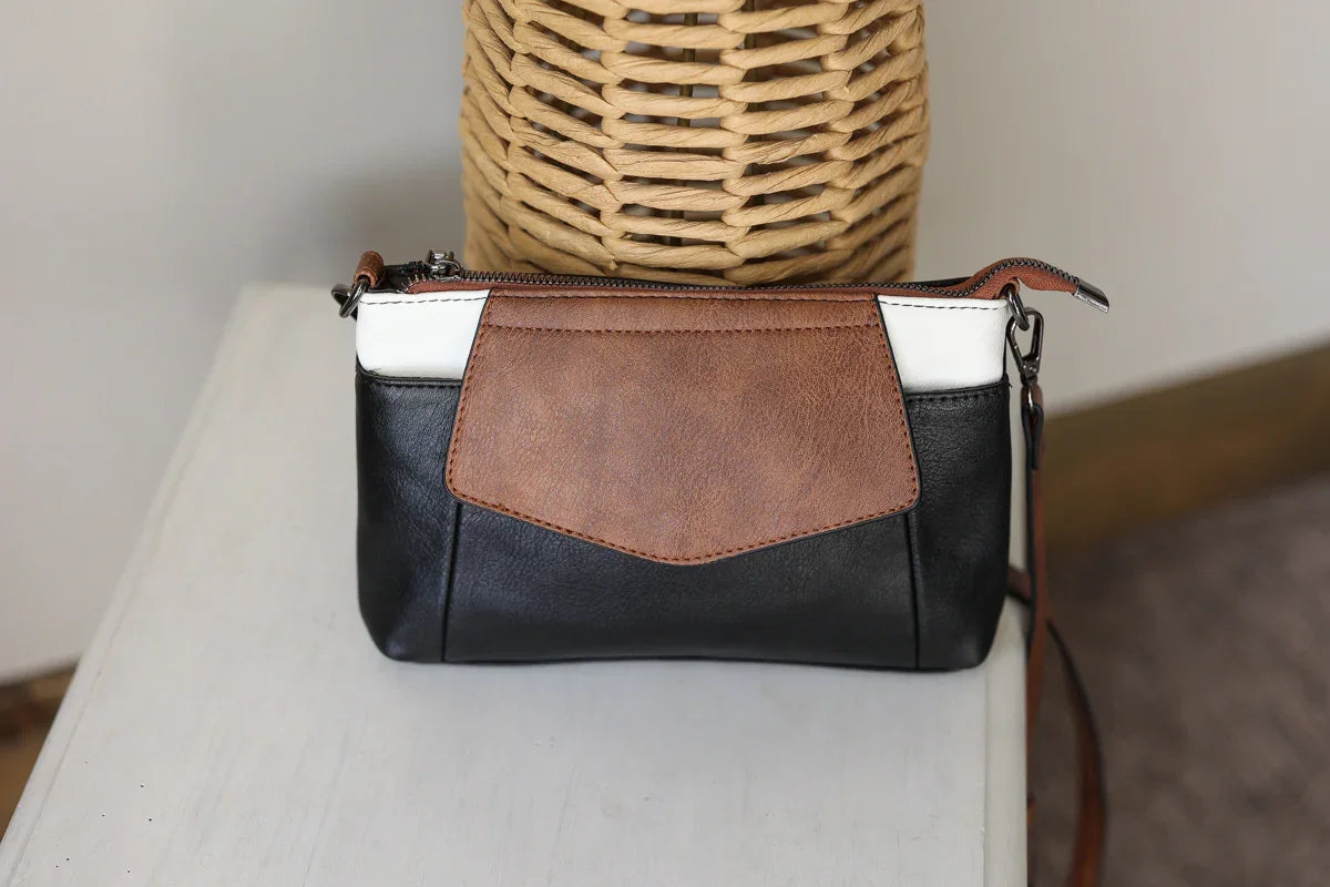 Black and brown handbag with a white section on a light surface.