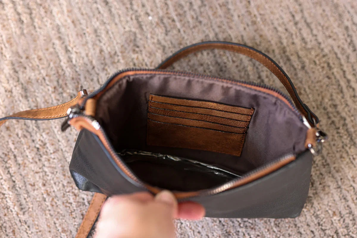 Hand holding an open brown leather handbag on a textured surface