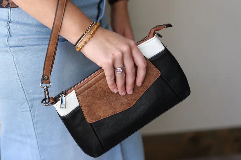 Person holding a black and brown handbag with light blue jeans and a patterned top.