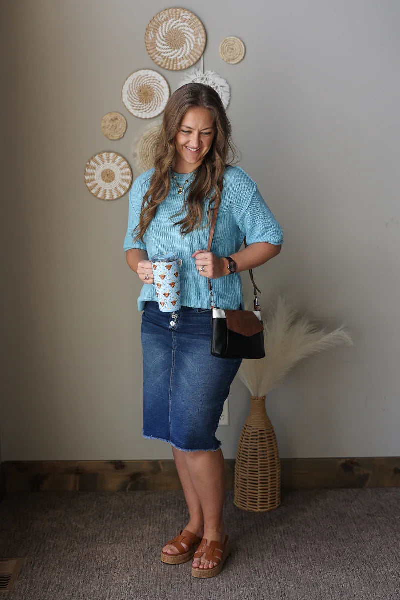 Woman holding a coffee cup and a handbag in a room with decorative wall art.