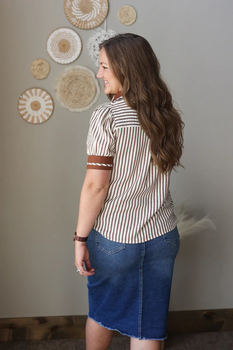 Woman wearing a striped shirt and blue skirt standing in front of decorative wall art.