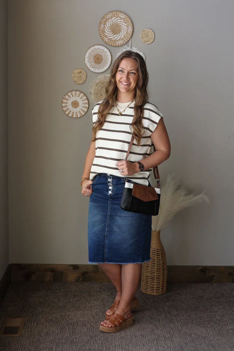 Woman wearing a striped shirt and denim skirt standing in a room with decorative wall art.