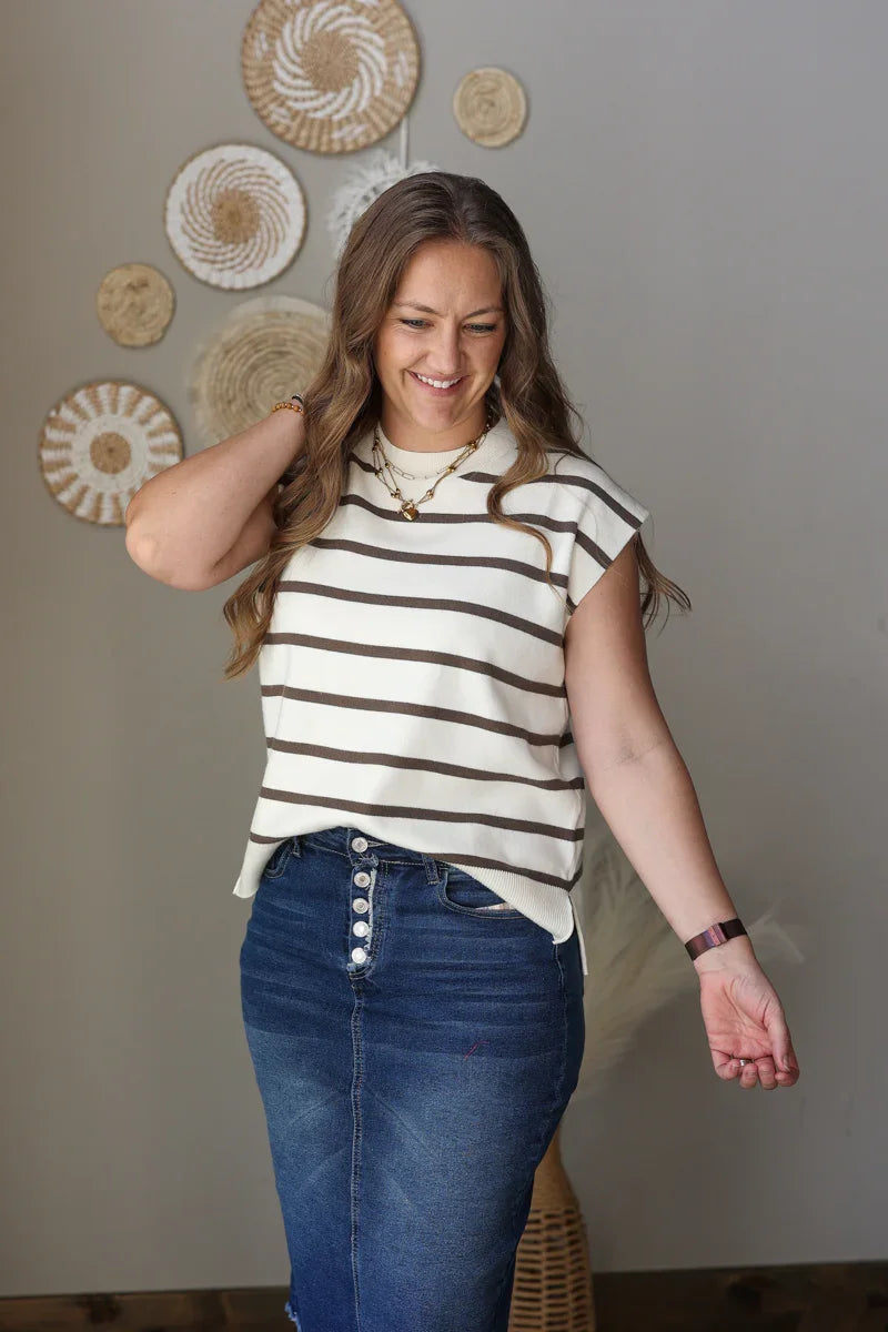 Woman wearing a striped shirt and blue jean skirt standing in front of decorative wall art.