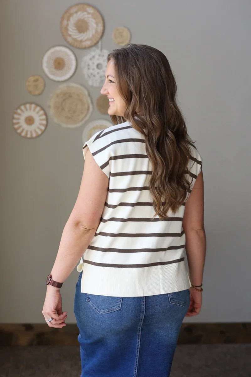 Woman wearing a striped shirt and blue jean skirt standing in front of decorative wall art.