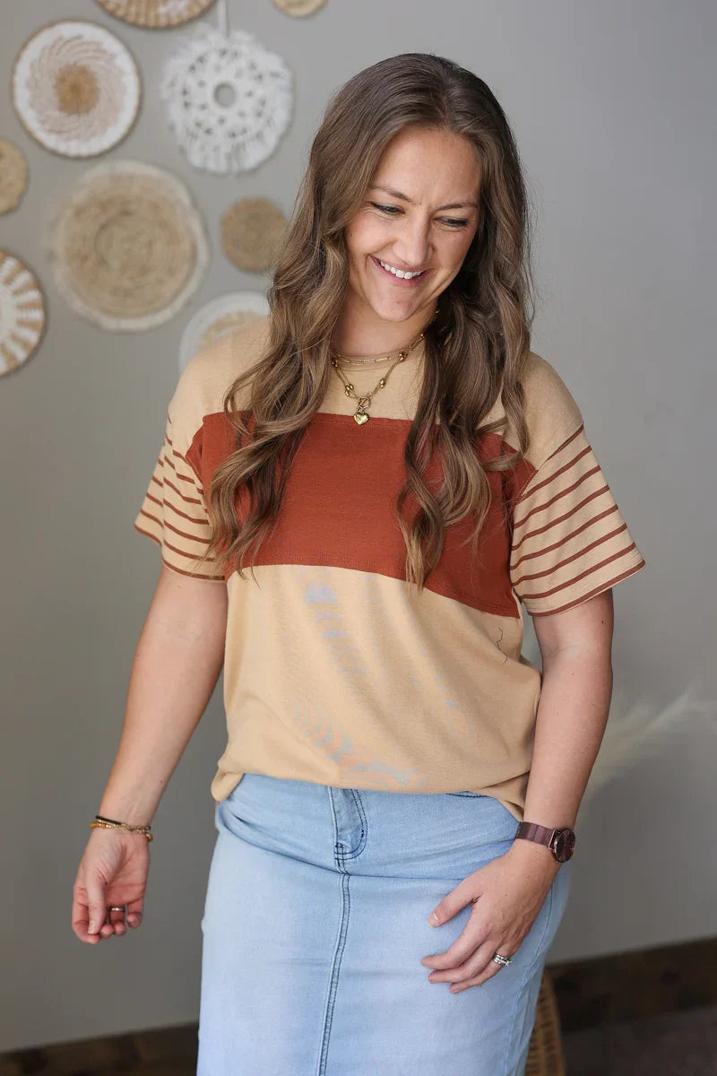 Woman wearing a beige and rust top with blue jean skirt in a room with decorative wall hangings.