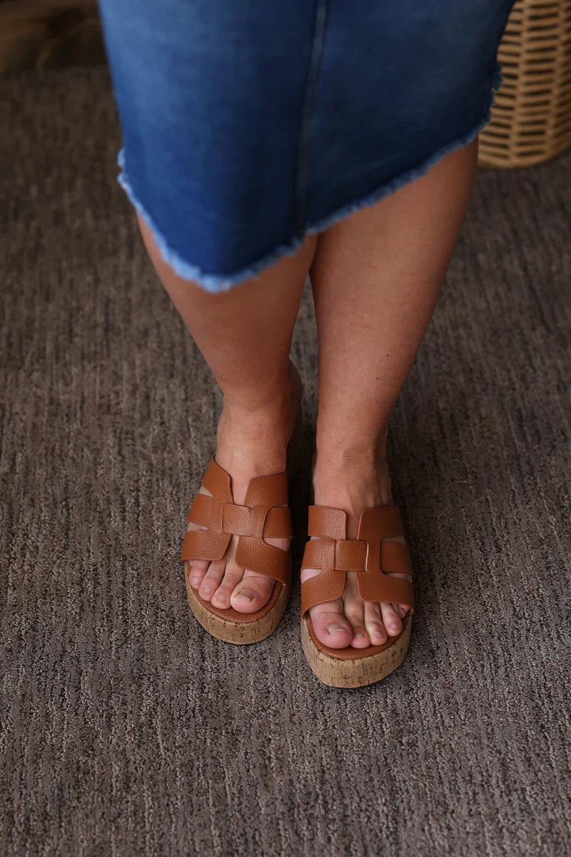 Brown woven sandals worn with a blue skirt on a textured surface