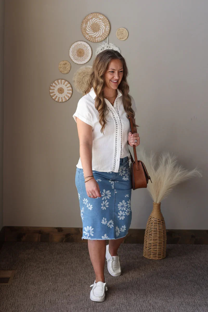 Woman in a white blouse and blue floral skirt standing in a room with decorative wall art.
