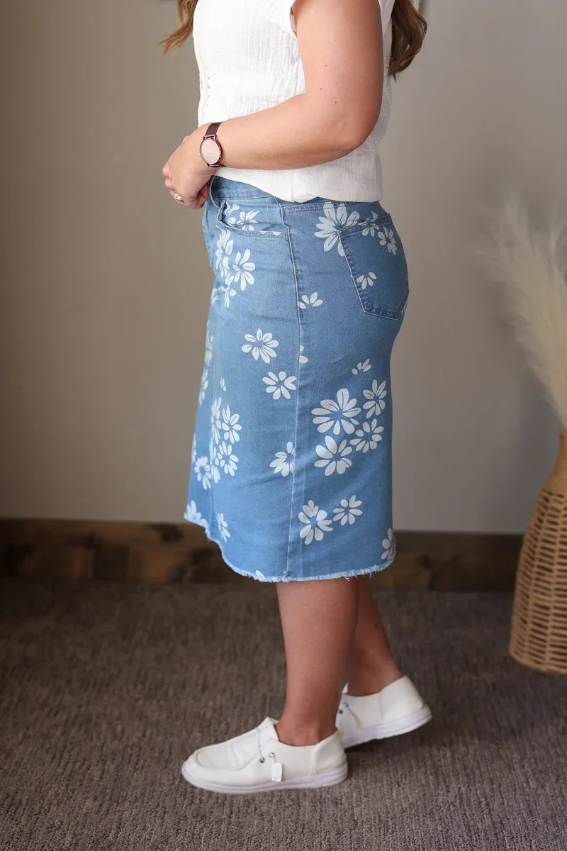 Person wearing a blue denim skirt with white floral patterns indoors.