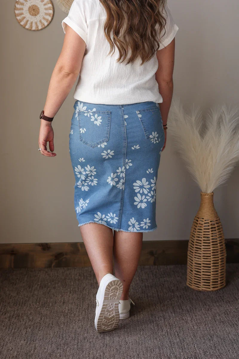 Person wearing a blue floral skirt with a white top in a room setting.