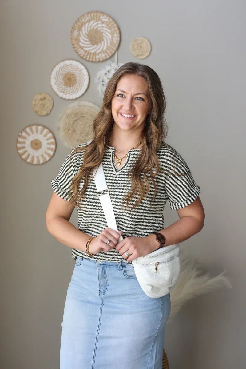 Woman wearing a striped shirt and light blue jeans, holding a white bag, with decorative wall art in the background.