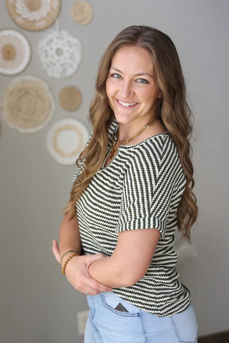 Woman wearing a dark green and white striped shirt with a neutral background