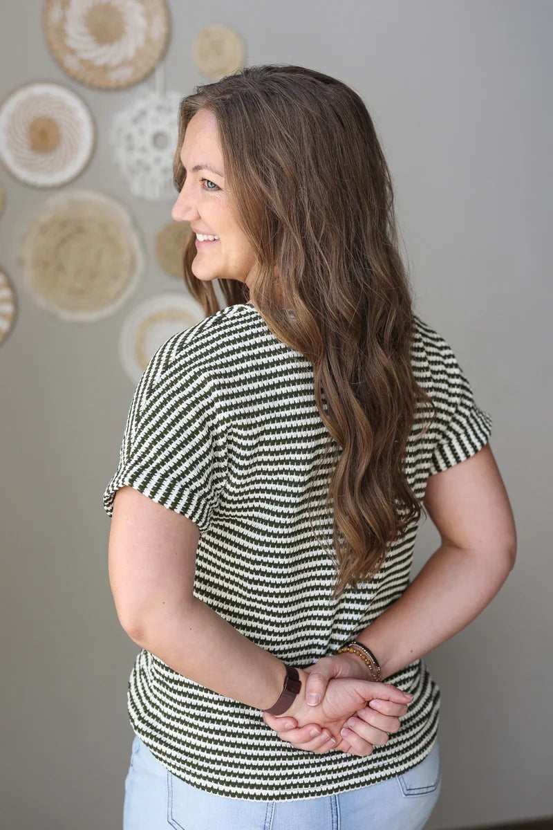 Woman wearing a dark green and white striped shirt with a neutral background