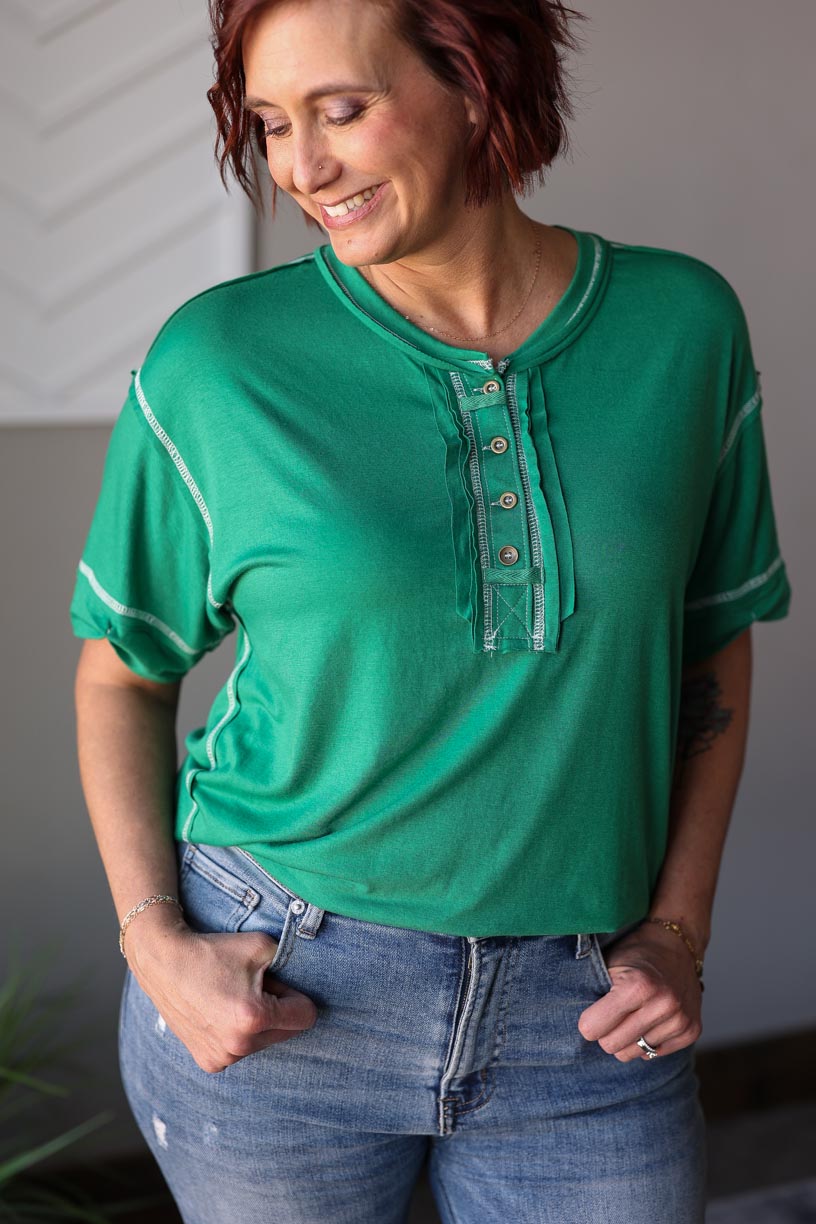 This cute Kelly Green Henley Top features a relaxed fit and pretty white contrast stitching. Perfect for everyday mom life, it's effortless and comfortable to wear, making it a go-to choice for any casual occasion. Easy to style and versatile, this top is a must-have addition to your wardrobe. Casual Spring Summer Top for women's everyday chic outfits.