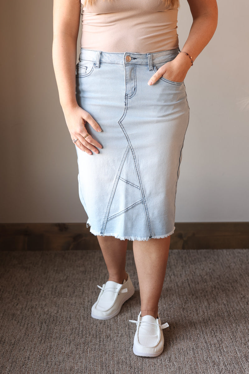 Person wearing a light blue denim skirt with a plain background