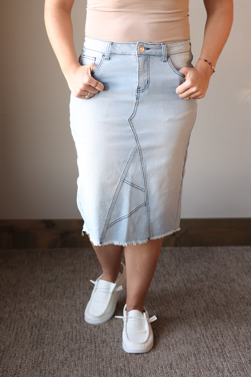 Person wearing a light blue denim skirt with a plain background