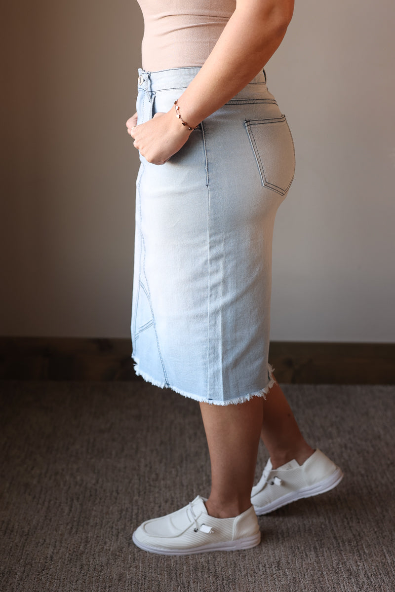 Person wearing a light blue denim skirt and white sneakers on a plain background