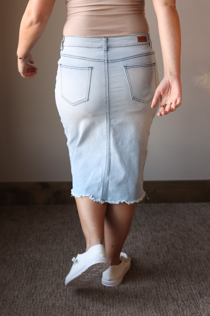 Person wearing a light blue denim skirt and white sneakers on a neutral background