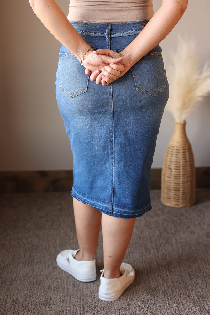 Person wearing a blue denim skirt with white sneakers in a room setting.