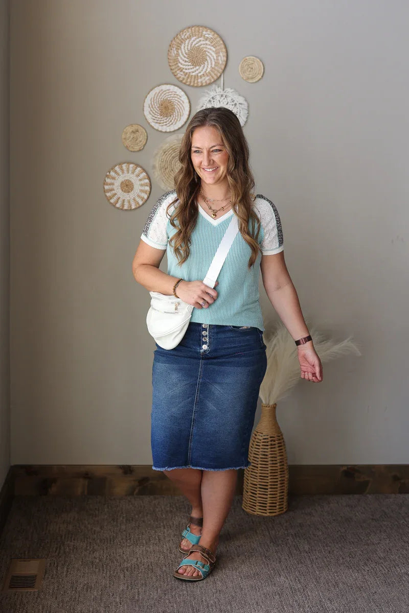Woman wearing a light blue top and denim skirt standing in a room with decorative wall art.