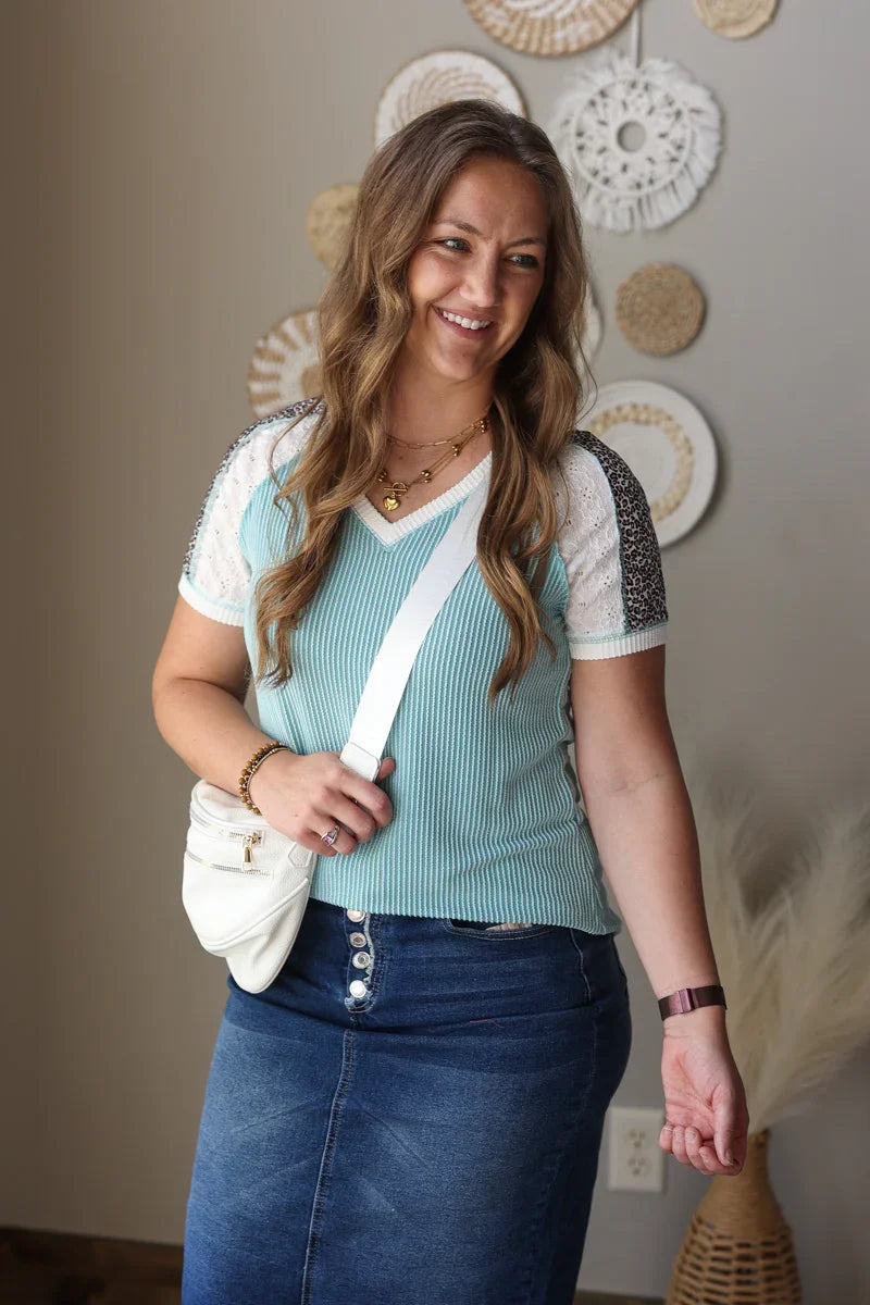 Woman wearing a light blue top and dark blue skirt with a white bag indoors.
