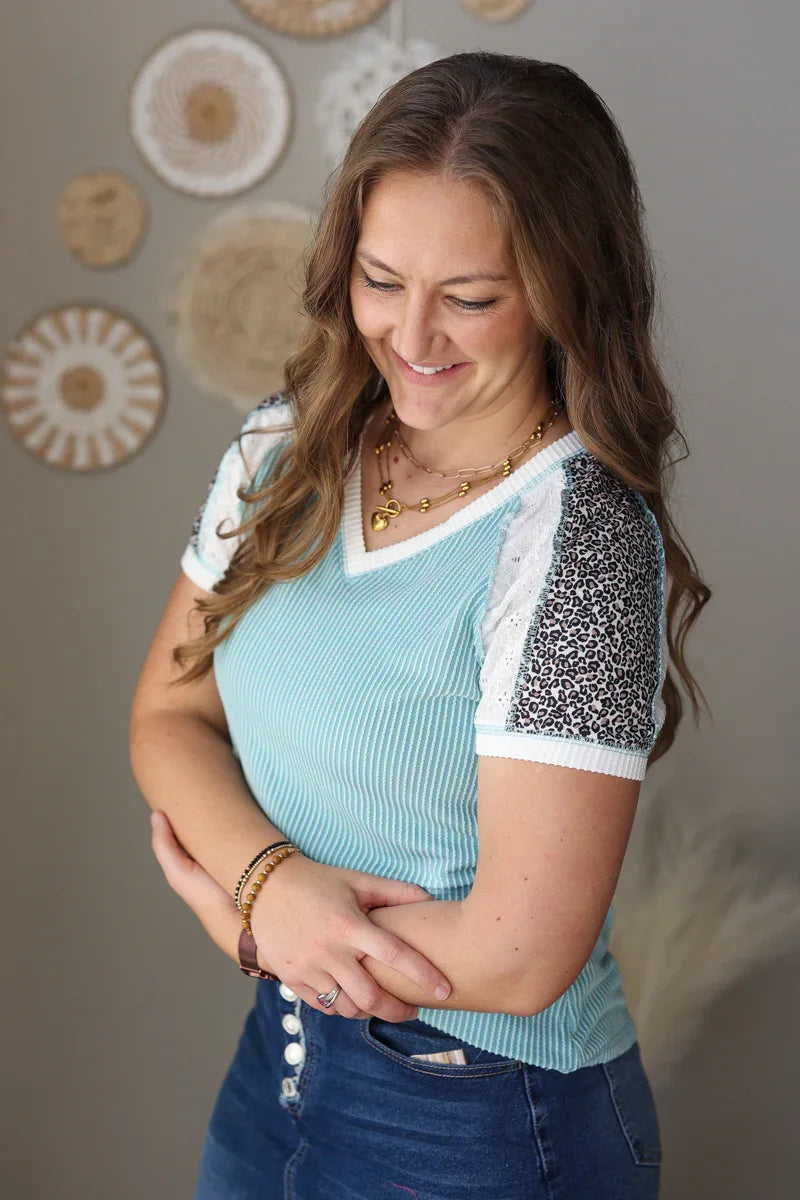 Woman wearing a light blue top with lace sleeves in a room with decorative wall art.