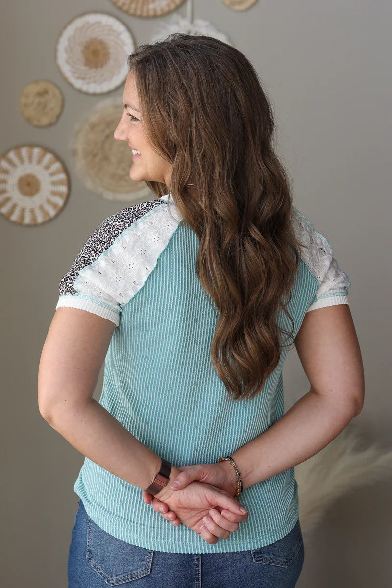 Woman wearing a light blue top with lace sleeves against a neutral wall.