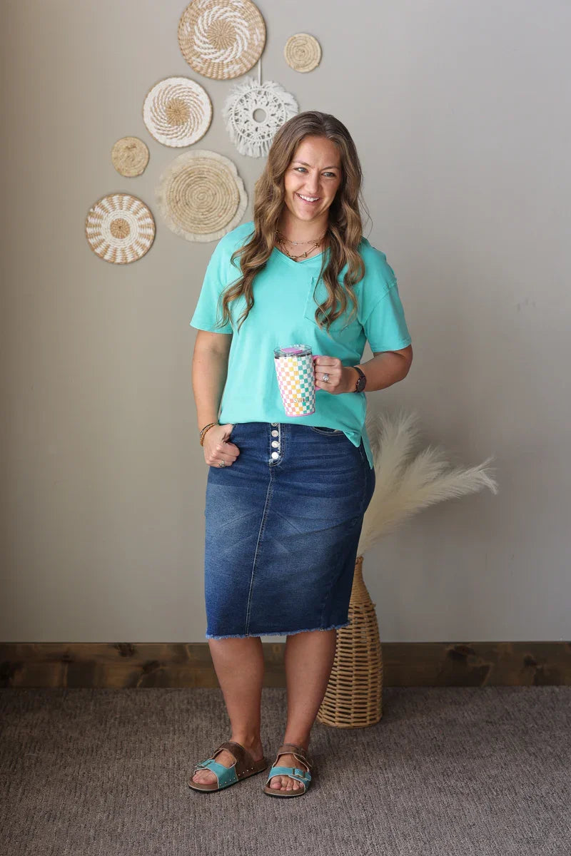 Woman in a teal shirt and denim skirt holding a polka dot cup against a wall with decorative plates.