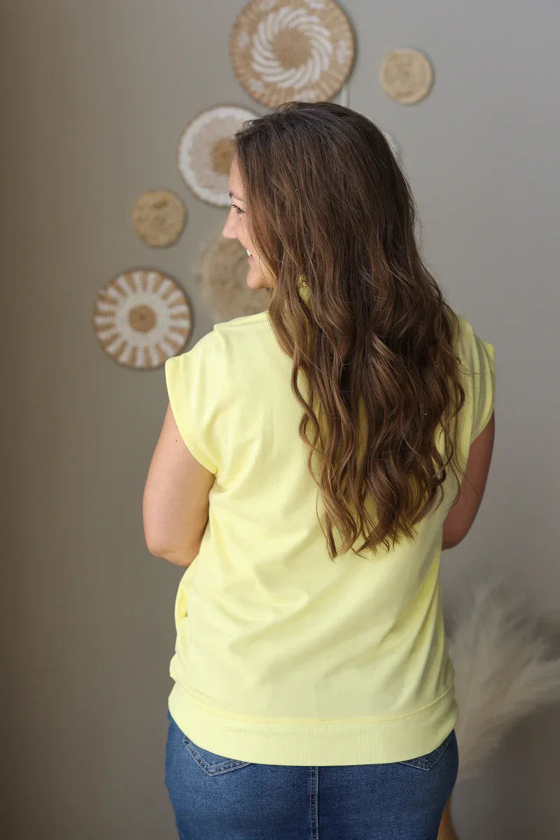 Woman wearing a yellow top and blue jean skirt standing in front of decorative wall art.