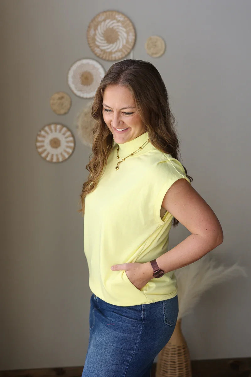 Woman wearing a yellow blouse and blue jean skirt standing against a wall with decorative plates.