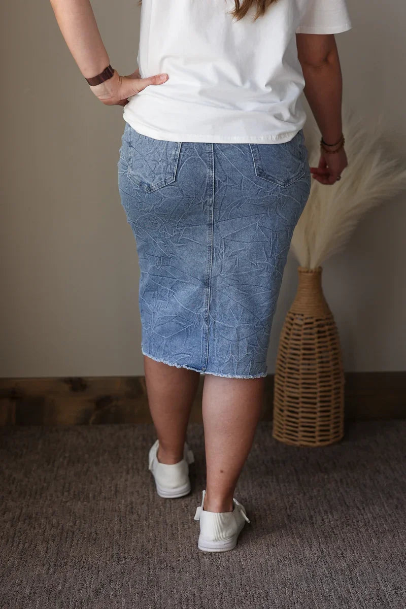 Person wearing a white t-shirt and blue denim skirt standing against a neutral background.