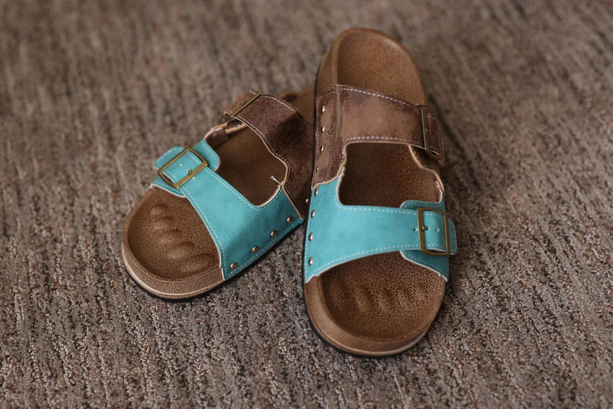 Pair of brown sandals with turquoise straps on a textured surface