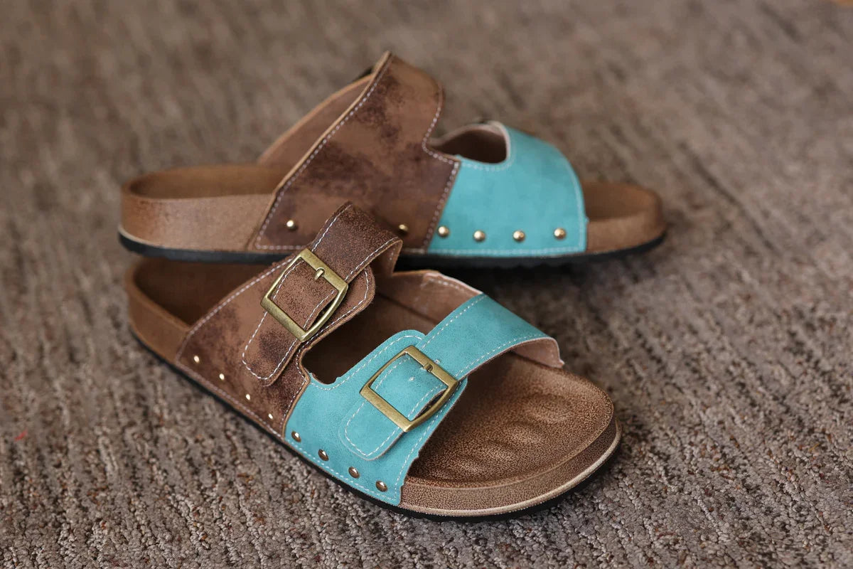 Pair of brown and turquoise sandals with gold buckles on a textured surface