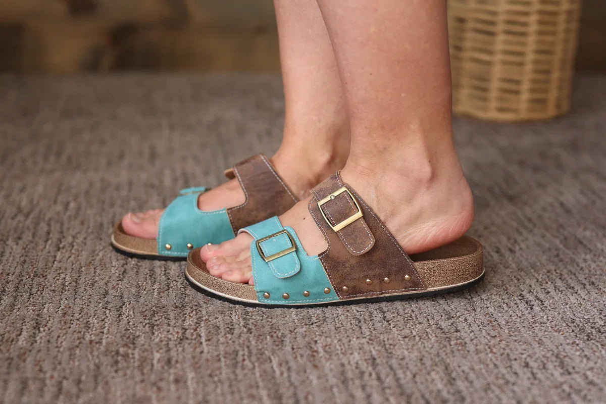 Brown and turquoise sandals worn on feet on a textured surface