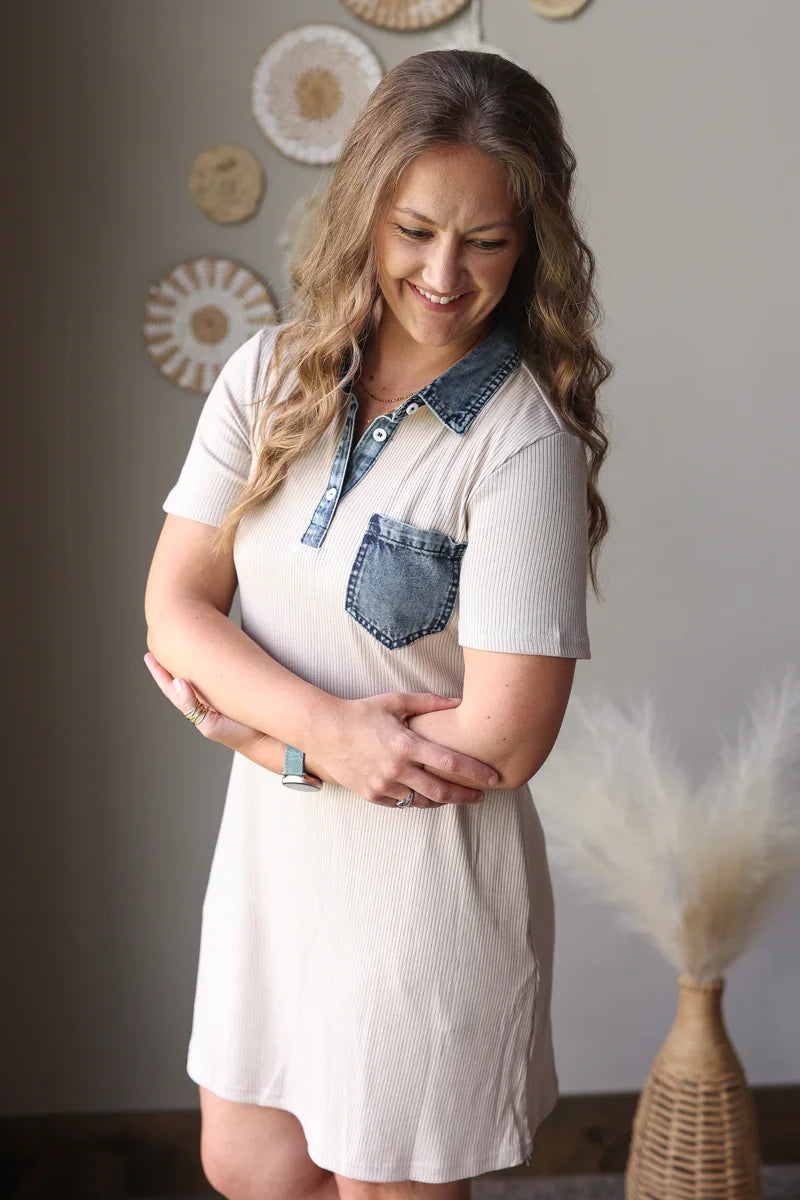 Woman wearing a tan dress with denim accents in a room with decorative elements.