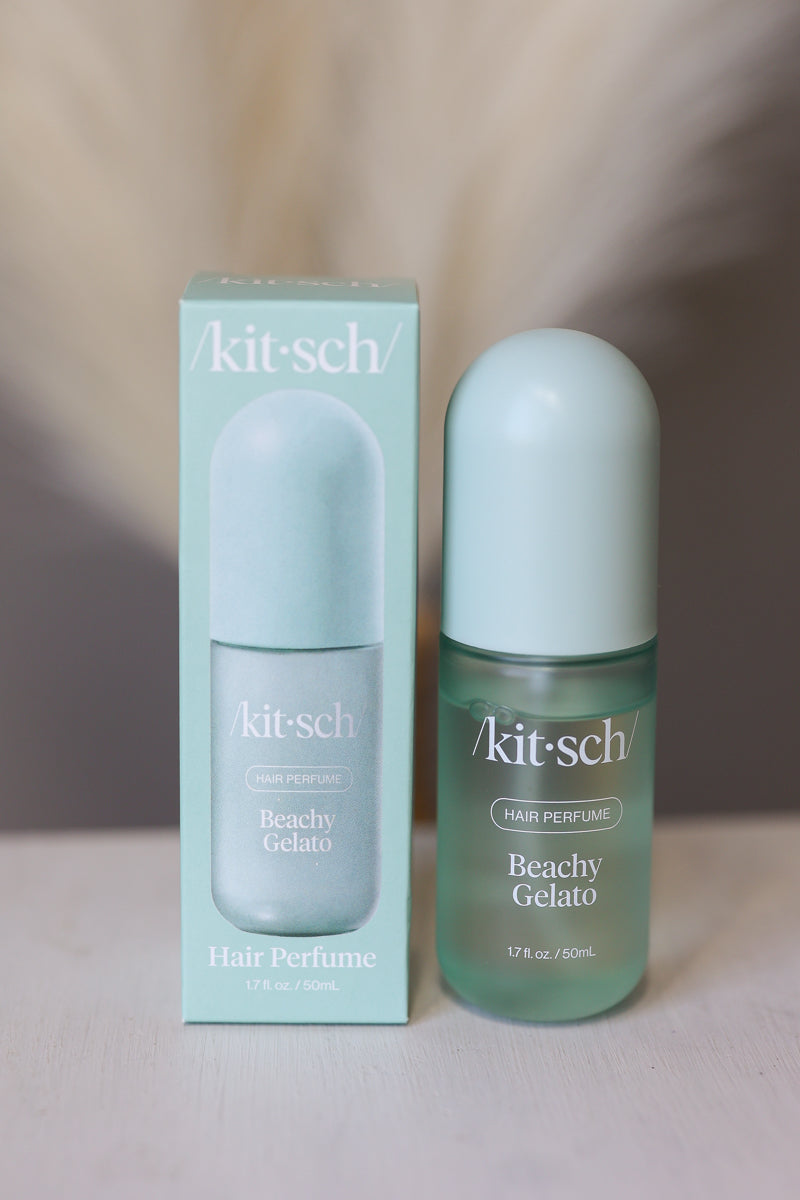 A bottle and matching box of kit-sch Beachy Gelato hair perfume, featuring a pale mint green color with white text, set against a soft beige background.