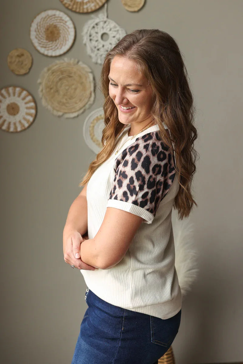 Woman wearing a white blouse with leopard print sleeves against a wall with decorative plates.