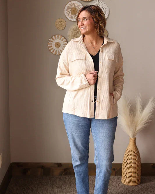 Woman wearing a beige shirt and blue jeans standing in a room with decorative wall art. Great shacket for easy cute and modest mom outfits at work or teachers.