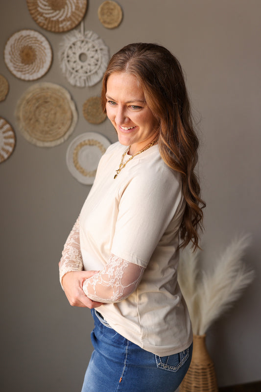 Woman wearing a cream blouse and blue jeans standing in front of decorative wall art.