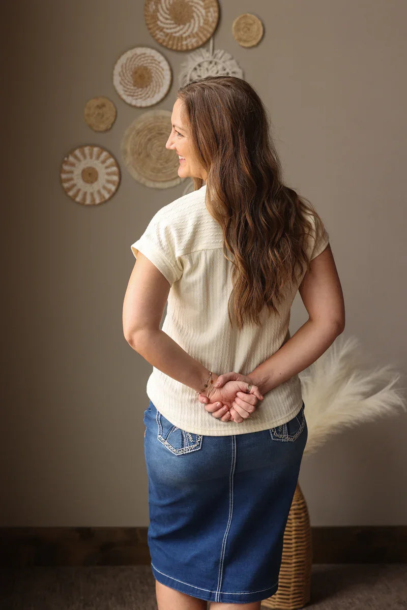 Woman standing with hands clasped in front of a wall with decorative plates.