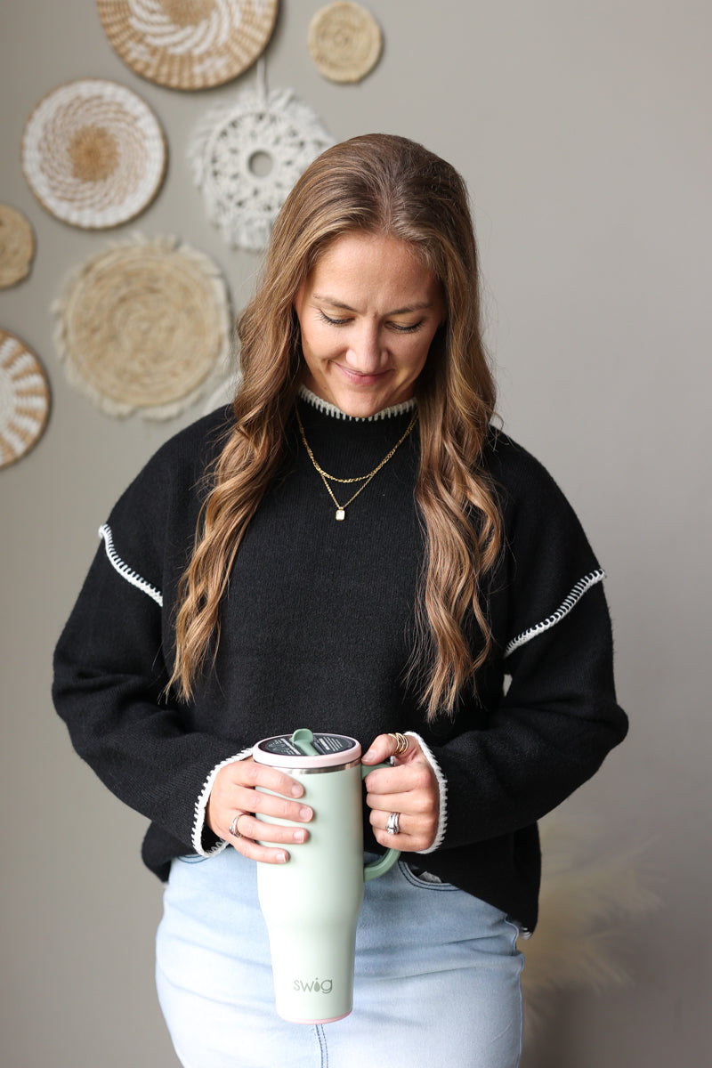 Close front view of a black mock neck sweater with light contrast shoulder stitching, worn with a light denim skirt.