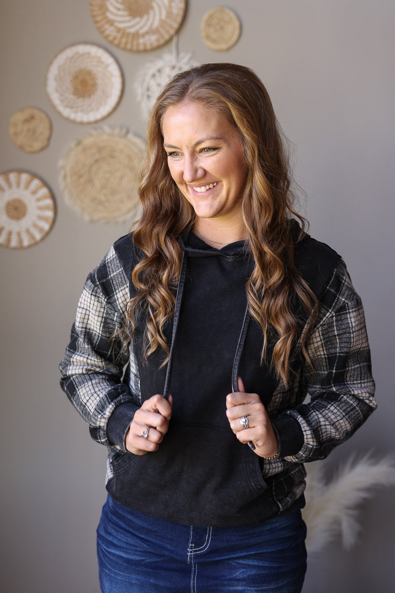 Black plaid sleeve hoodie shown with hands in the front pocket and a dark denim skirt.