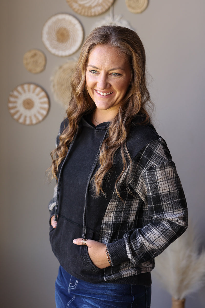 Angled front view of a black pullover hoodie with grey plaid sleeves and solid black cuffs.
