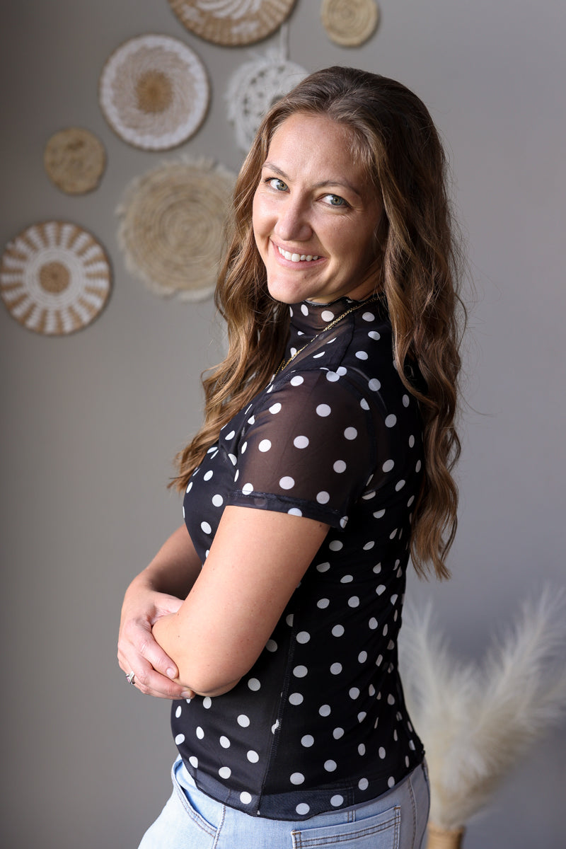 Woman wearing a black top with white polka dots in a room with decorative wall hangings.