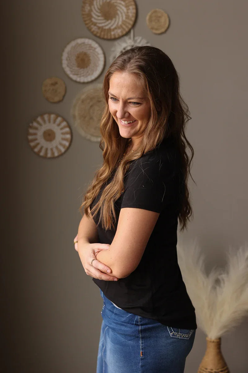Woman in a black shirt and blue jean skirt standing against a wall with decorative plates.