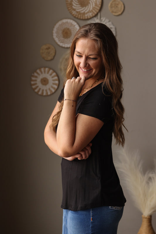 Woman wearing a black t-shirt and blue jean skirt standing against a neutral wall with decorative elements.