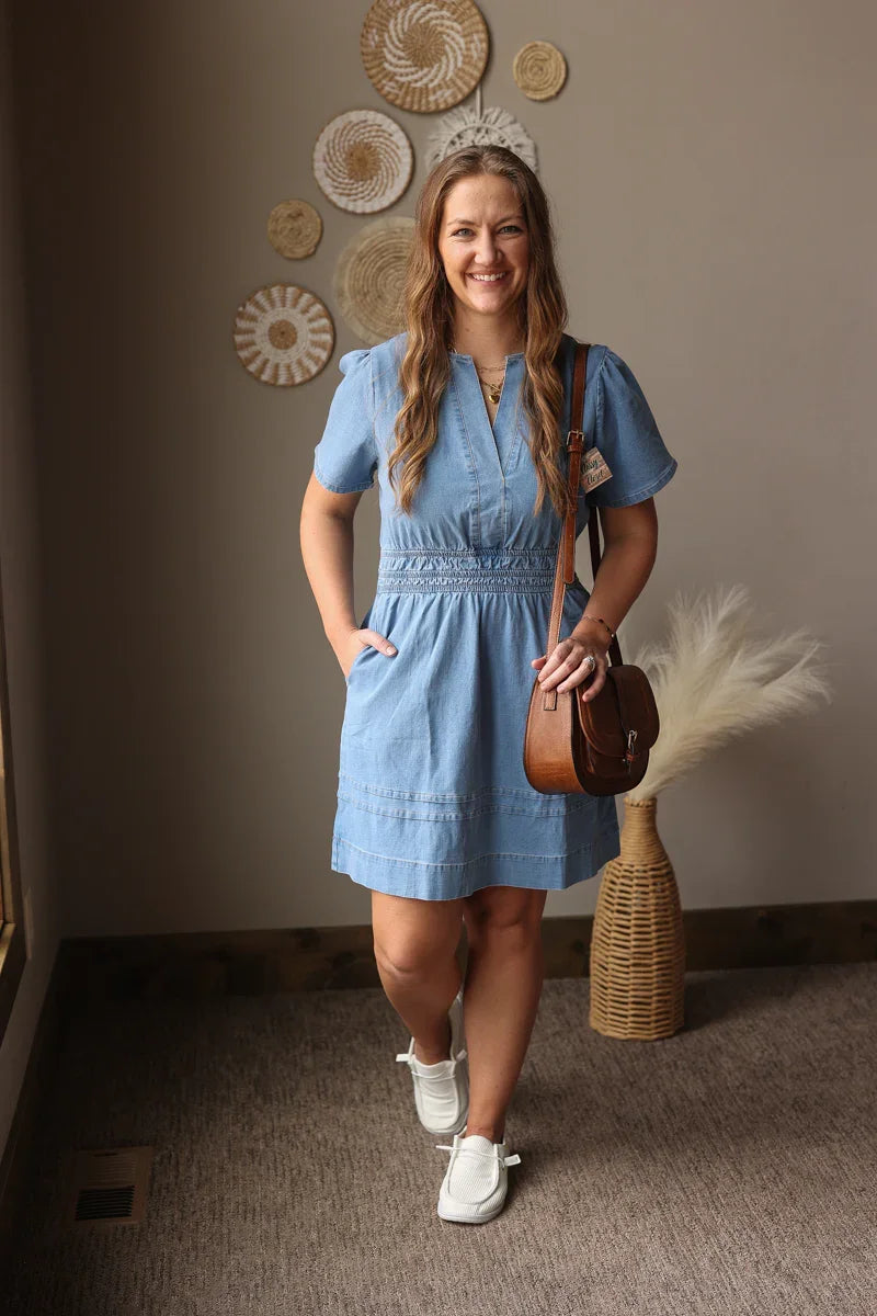 Woman in a blue dress standing in a room with decorative wall art and a vase.