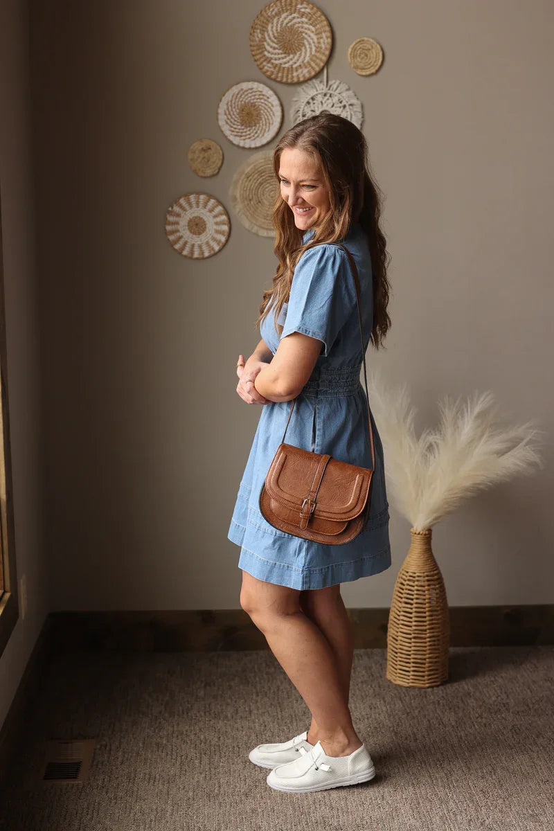 Woman in a blue dress with a brown bag standing in a room with decorative wall art.
