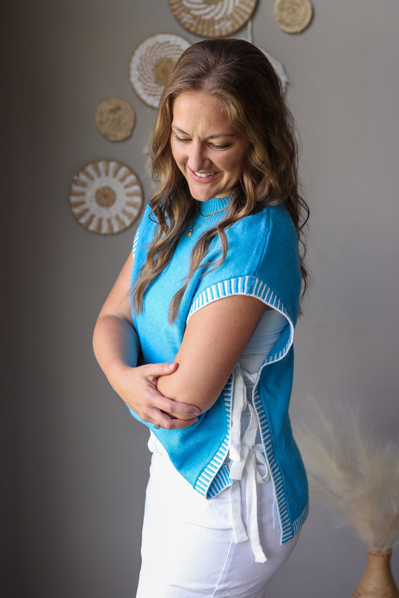Woman wearing a blue top with white trim against a gray wall with decorative plates.